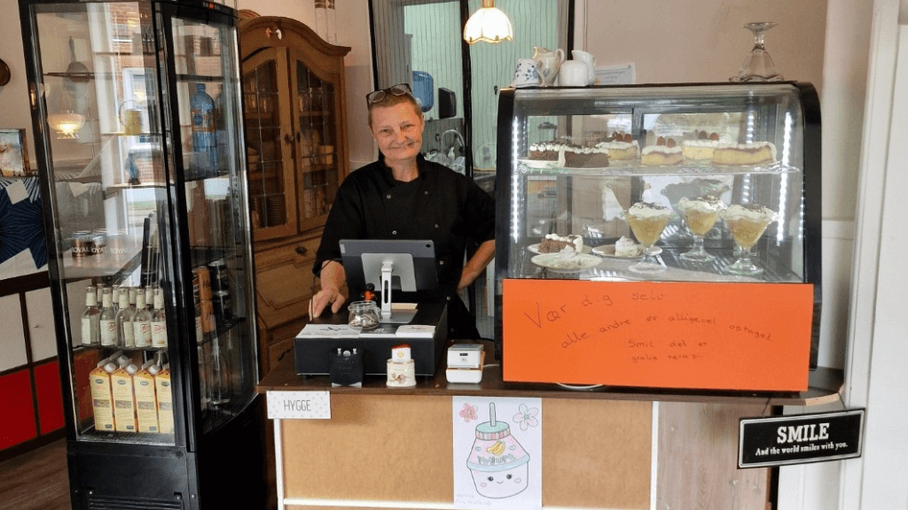 Woman in black clothing behind the counter with display cases and arranged cakes.